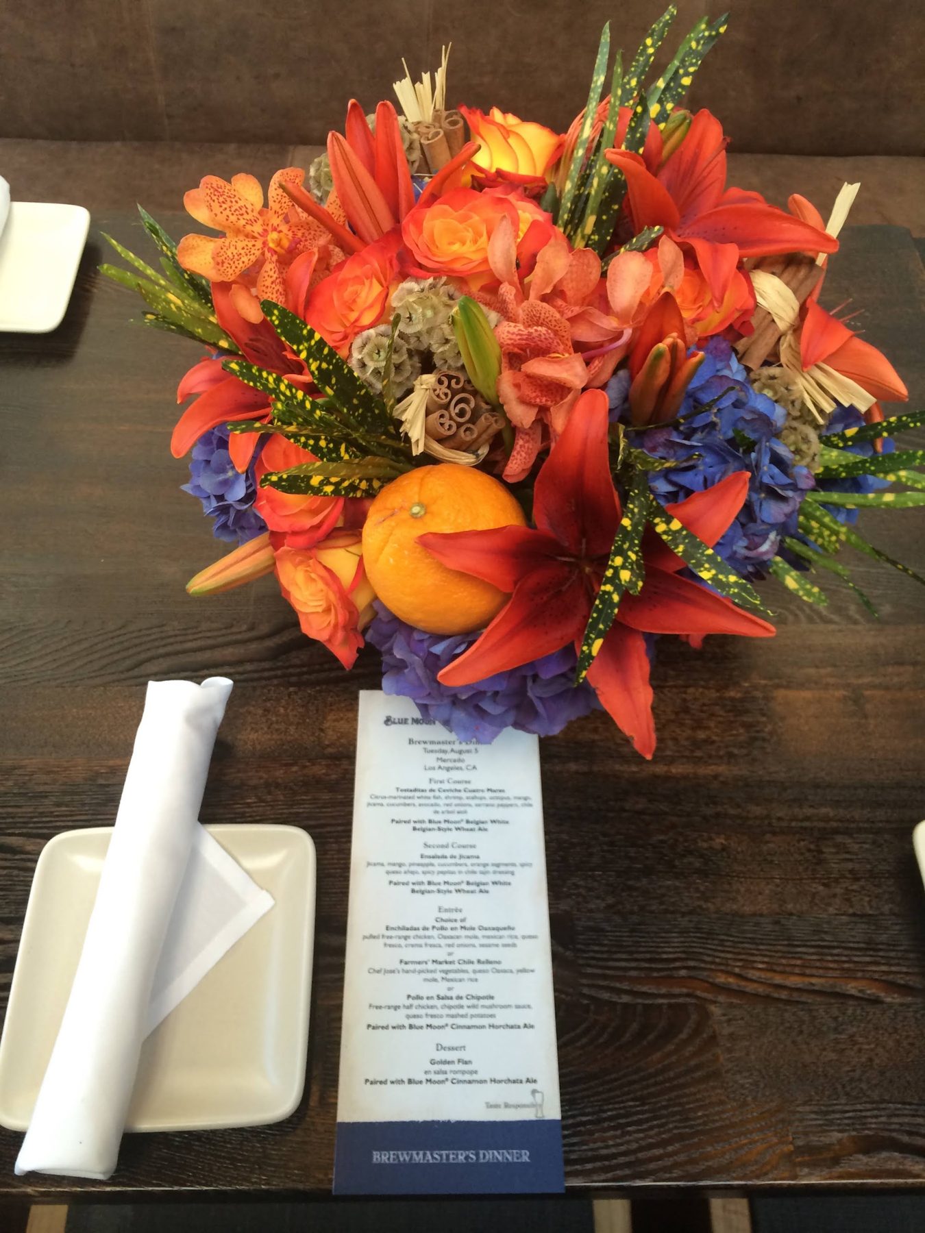 Place setting with a Blue Moon Brewmaster's Dinner menu and an orange floral centerpiece