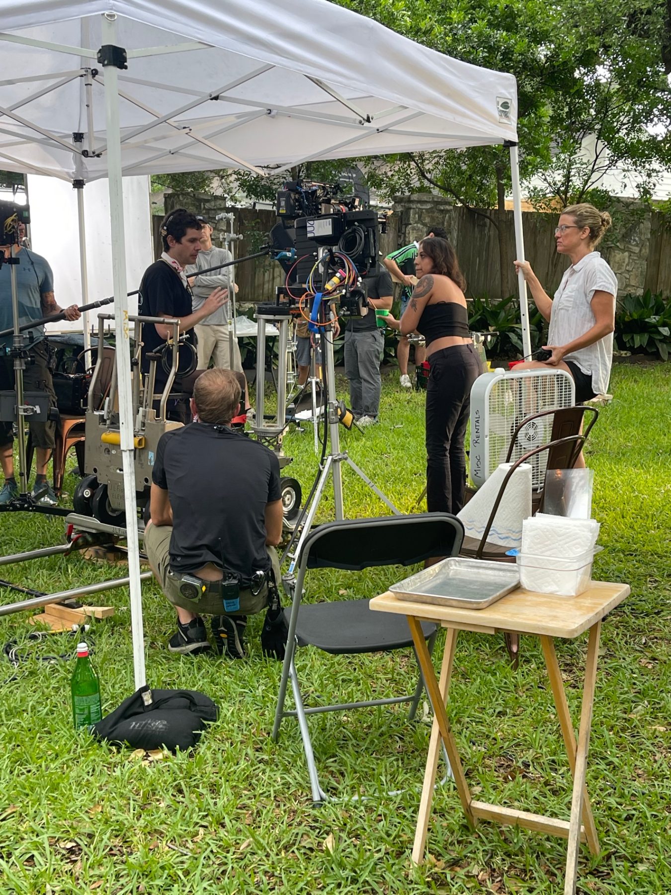 A film crew working around a camera under a white canopy in a garden