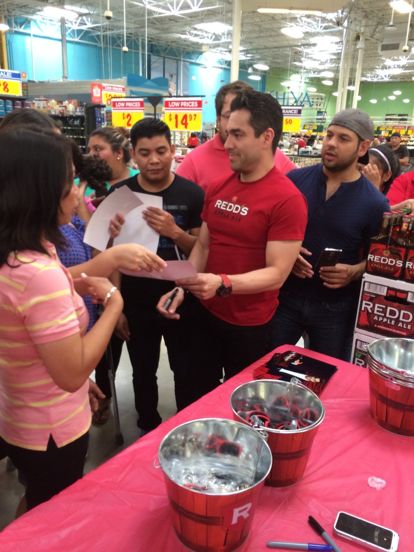 A guest in a Redd's Apple Ale shirt signing autographs at a table with Redd's ice buckets inside a grocery store
