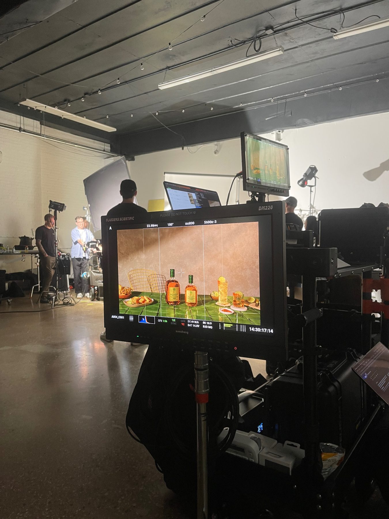 A studio crew and camera equipment behind a monitor displaying Buchanan's bottles and cocktails