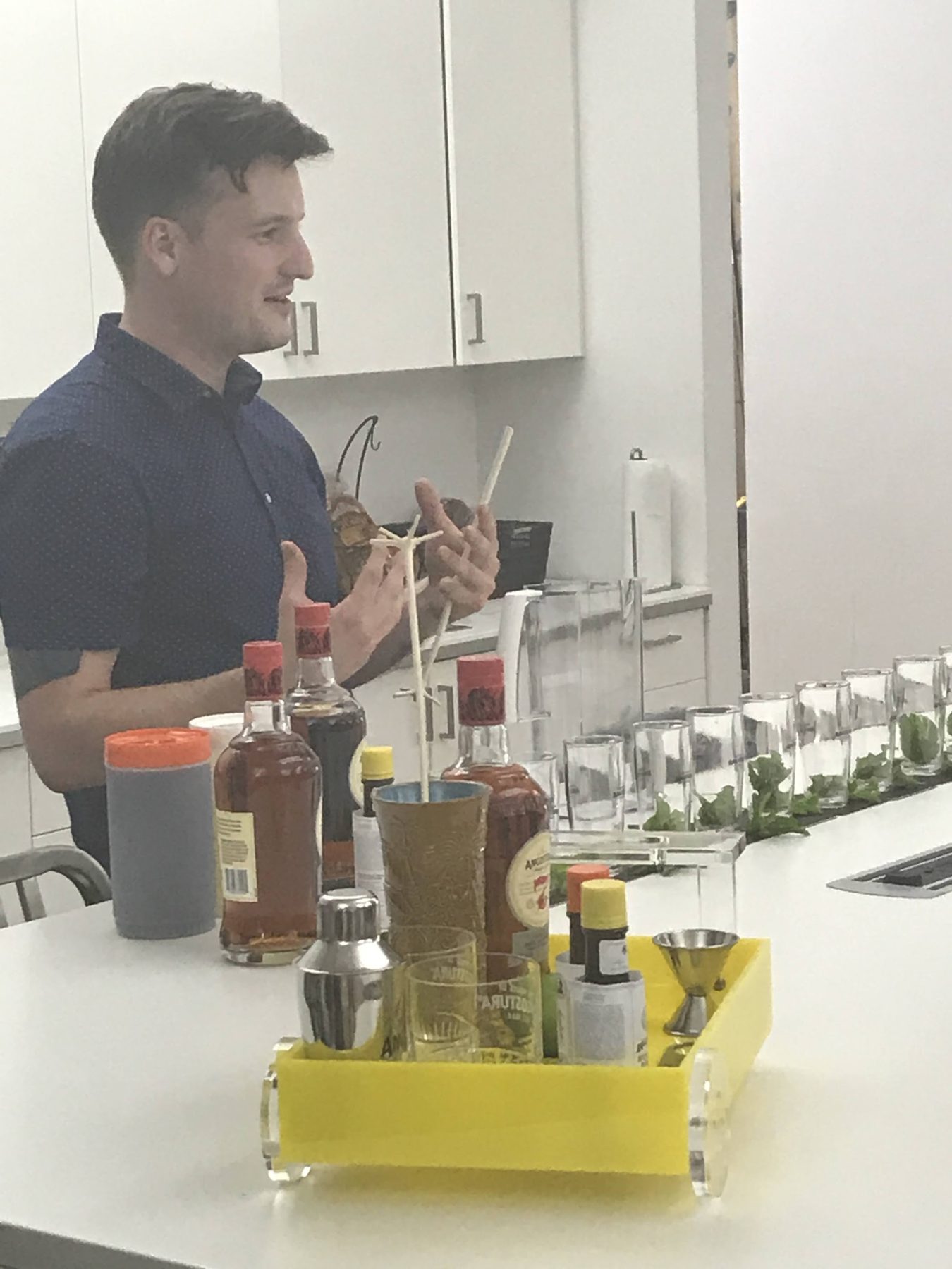 A bartender explaining a cocktail beside a yellow tray of ANGOSTURA bitters and bar tools