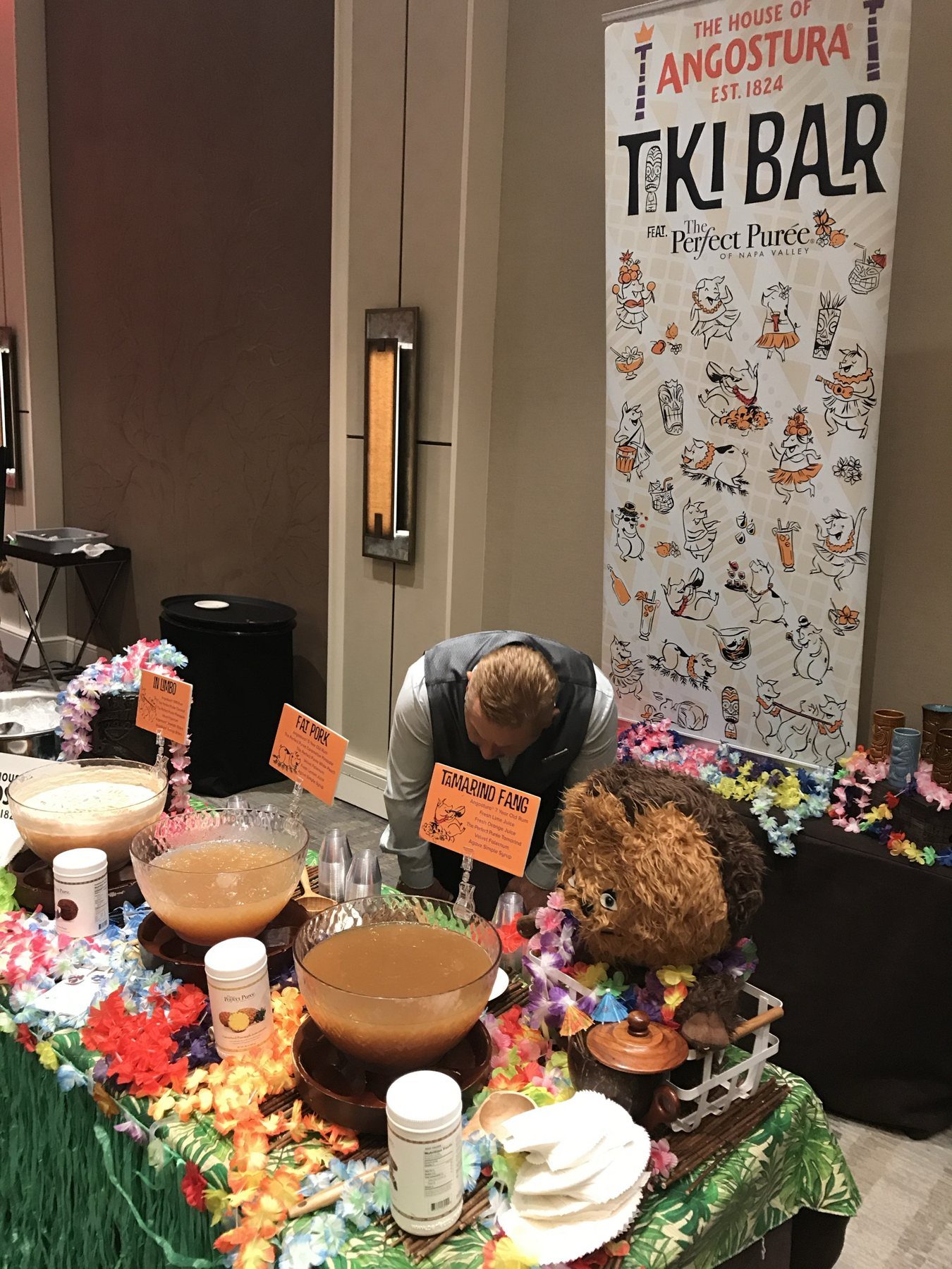 A tiki punch station with three punch bowls, leis and a House of Angostura Tiki Bar banner