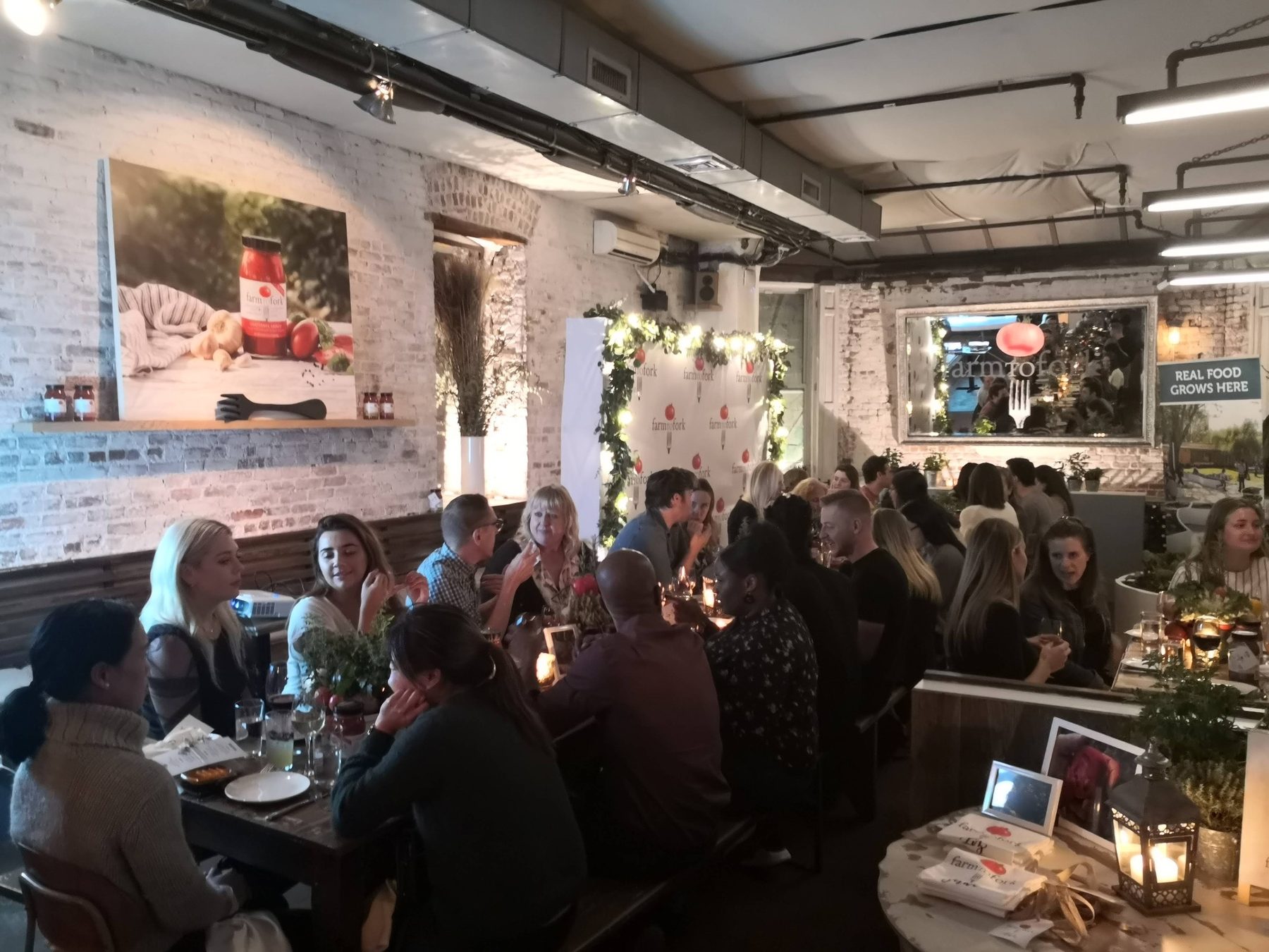 Guests at candlelit tables at a FarmToFork media dinner with a branded backdrop and step-and-repeat