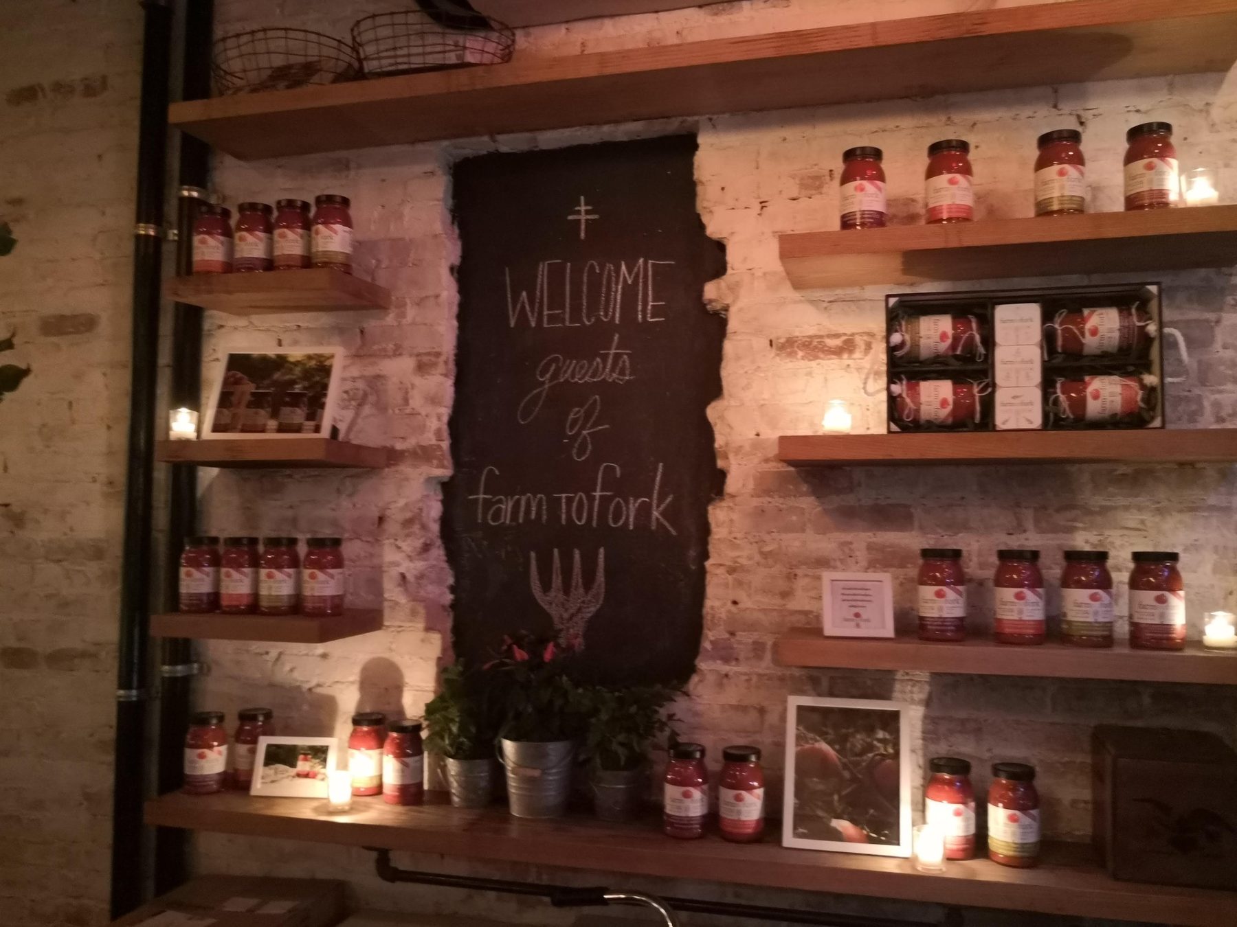 Wooden shelves lined with FarmToFork pasta sauce jars around a 'Welcome guests of farmtofork' chalkboard