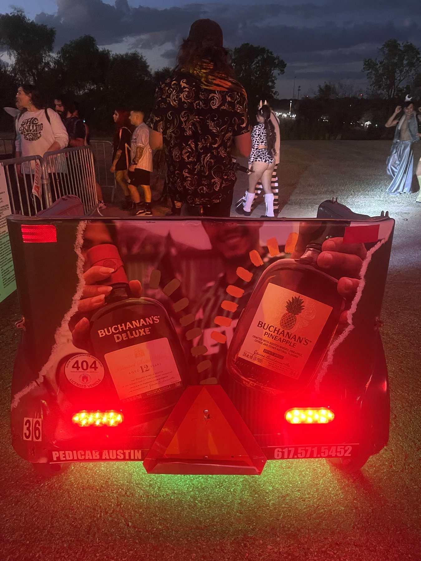 The back of a pedicab with Buchanan's DeLuxe and Buchanan's Pineapple bottle artwork, lit by tail lights