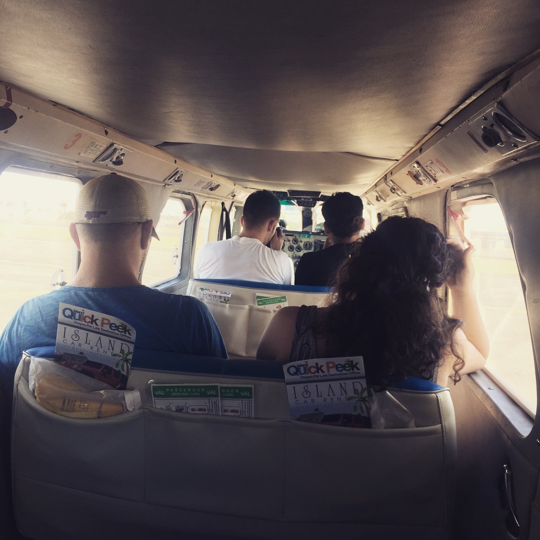Passengers inside a small propeller plane, seen from the back row, with Vieques Air Link seat cards