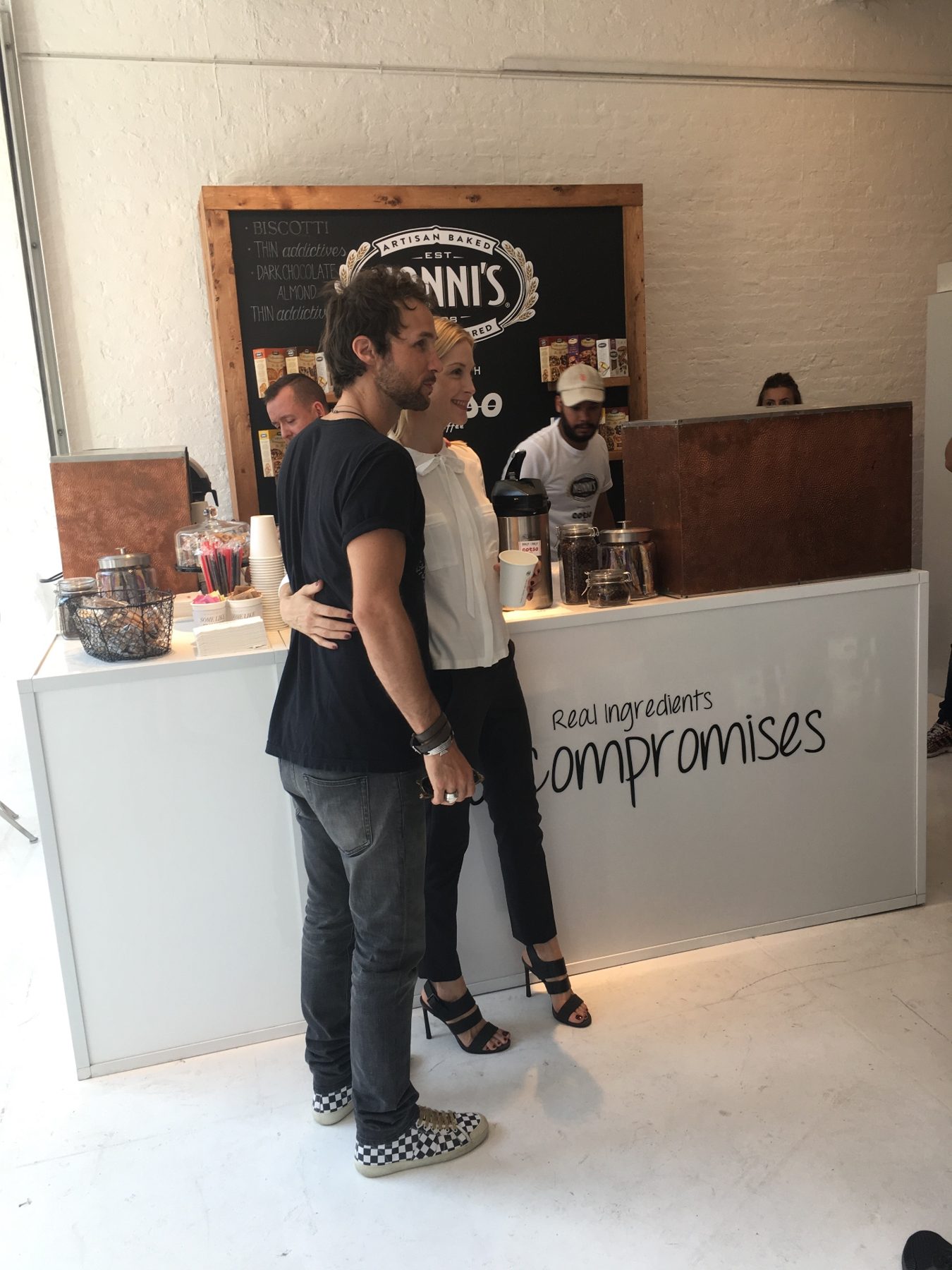Two guests posing together in front of the Nonni's café counter, one holding a coffee cup