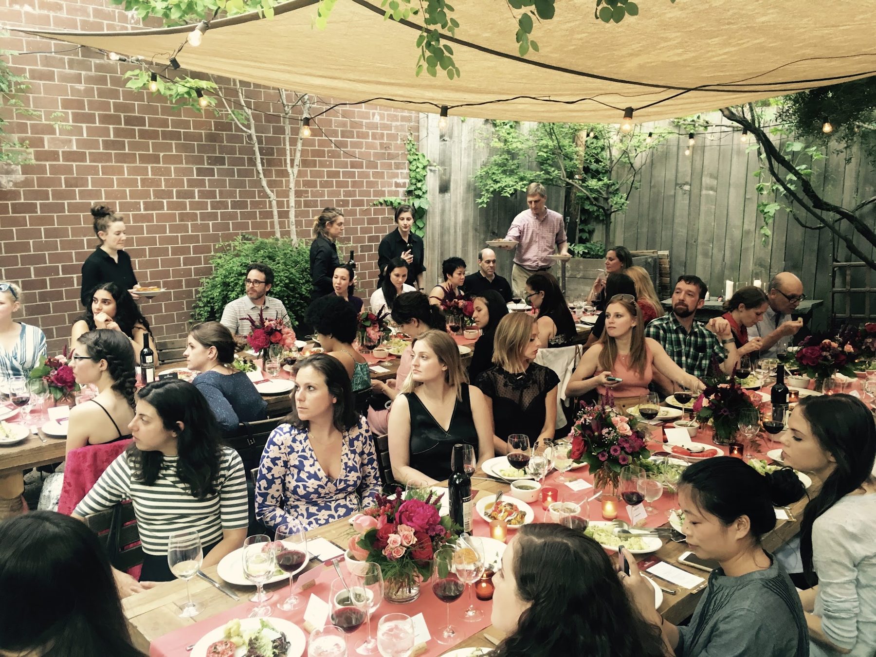 Guests seated at long tables under a canopy in a garden courtyard