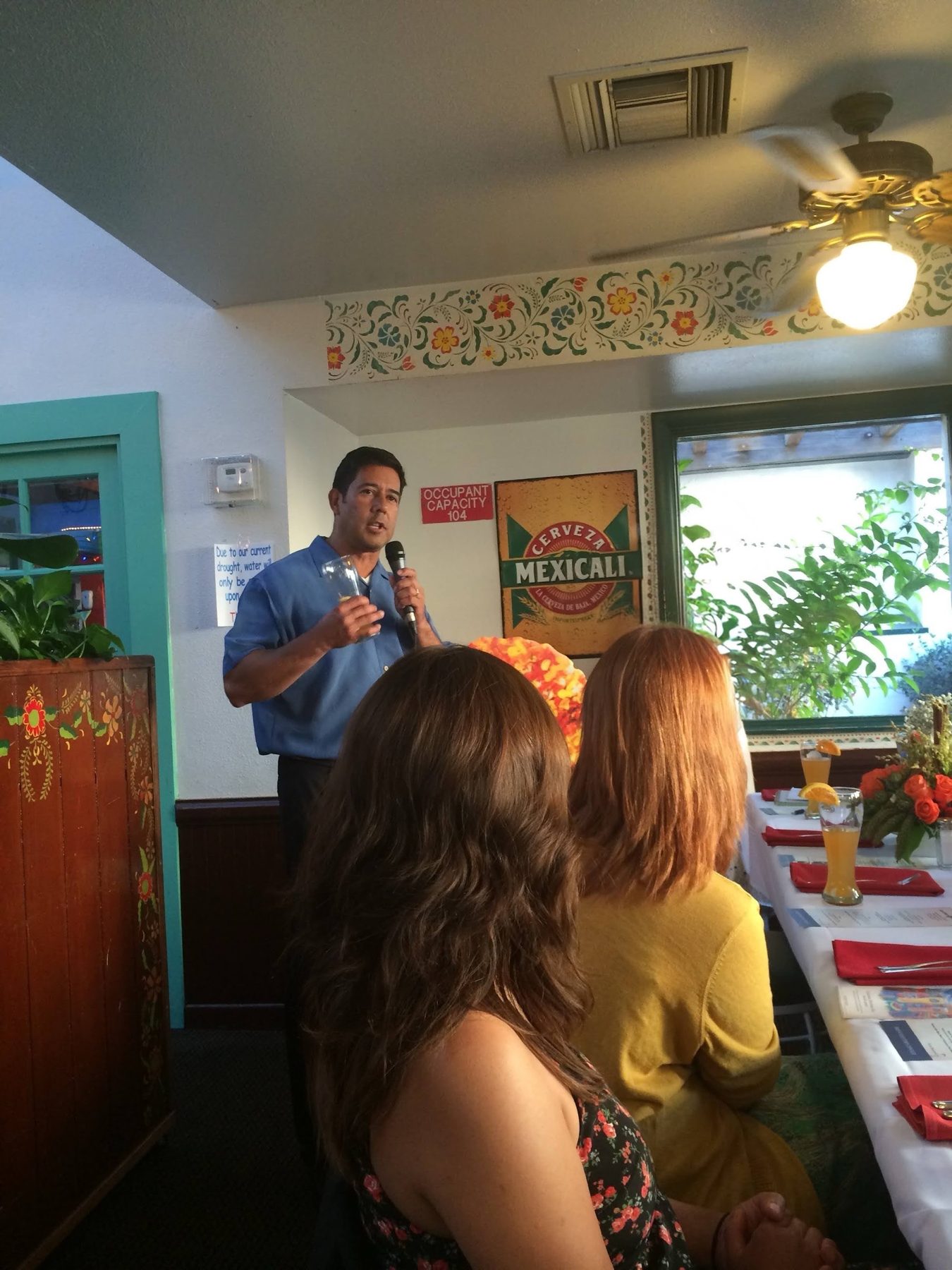 A presenter with a microphone speaking to journalists at a long table