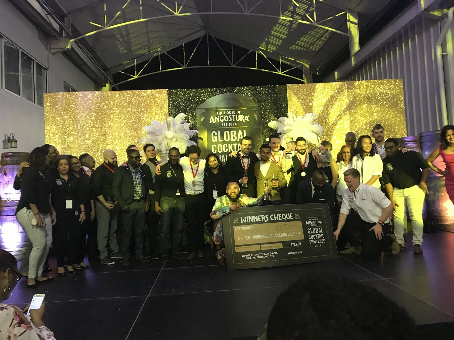 Finalists, judges and hosts on stage in front of a Global Cocktail Challenge backdrop with an oversized winner's cheque