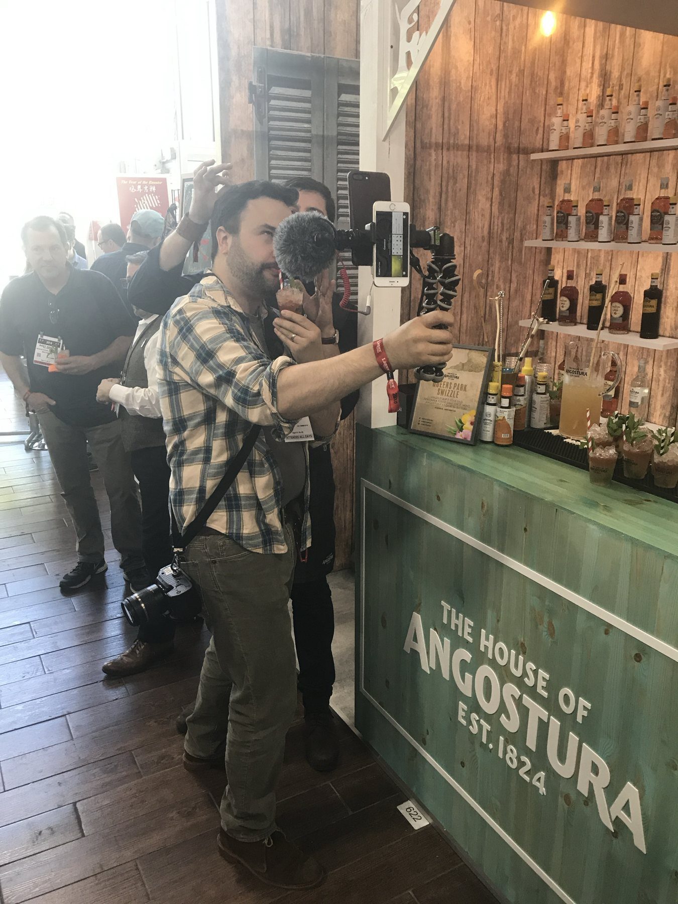 A content creator filming with a phone rig at a green-and-wood House of Angostura bar serving Queens Park Swizzles