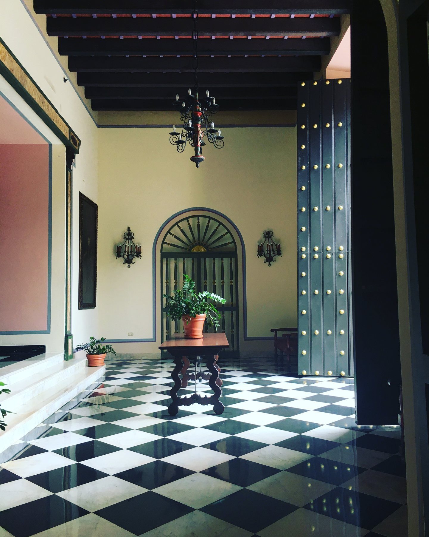 A colonial interior with a black-and-white checkered marble floor, a wrought-iron chandelier and tall studded doors