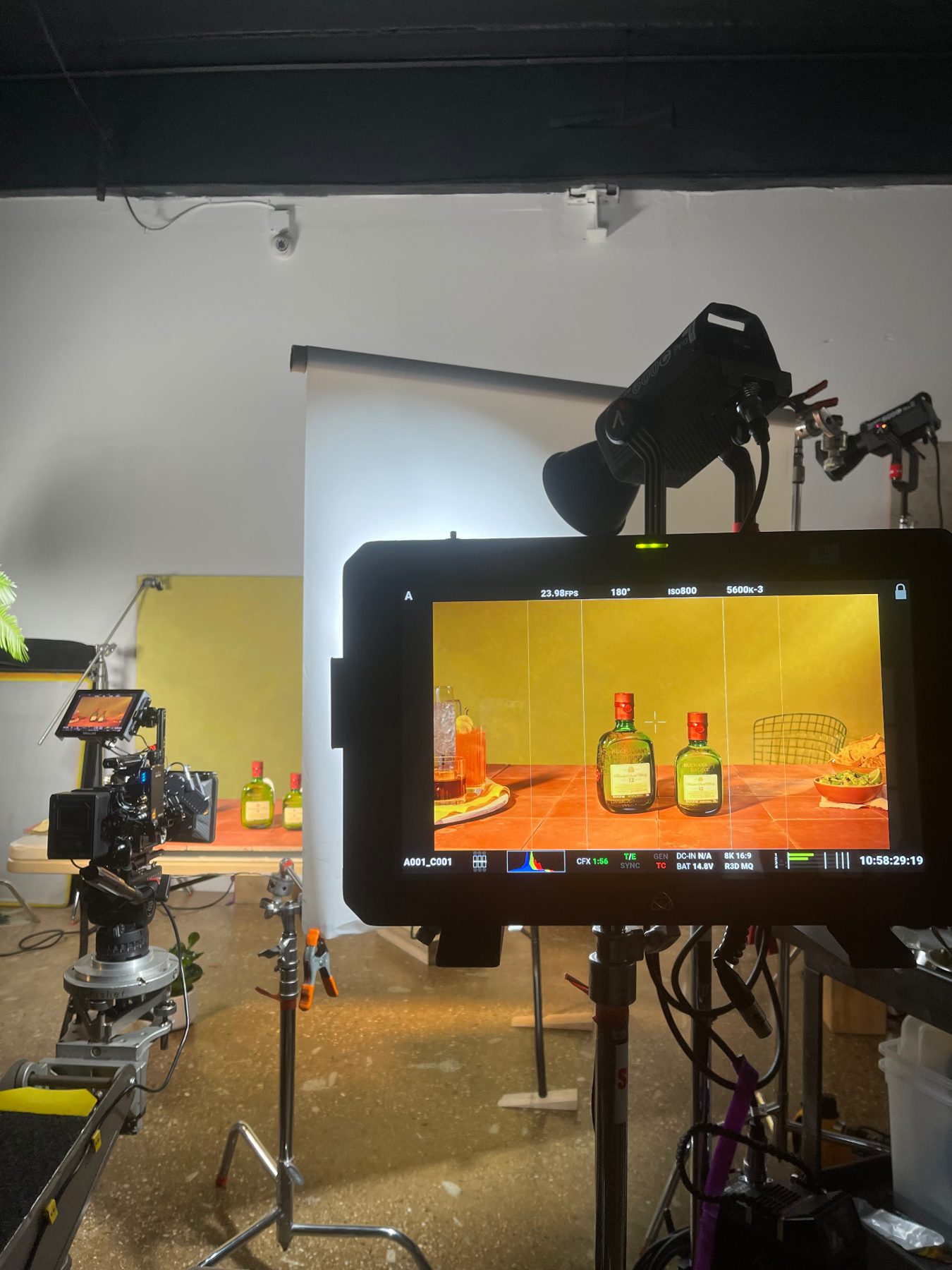 A production monitor showing Buchanan's bottles and cocktails on a colorful tabletop, with a camera rig beside it