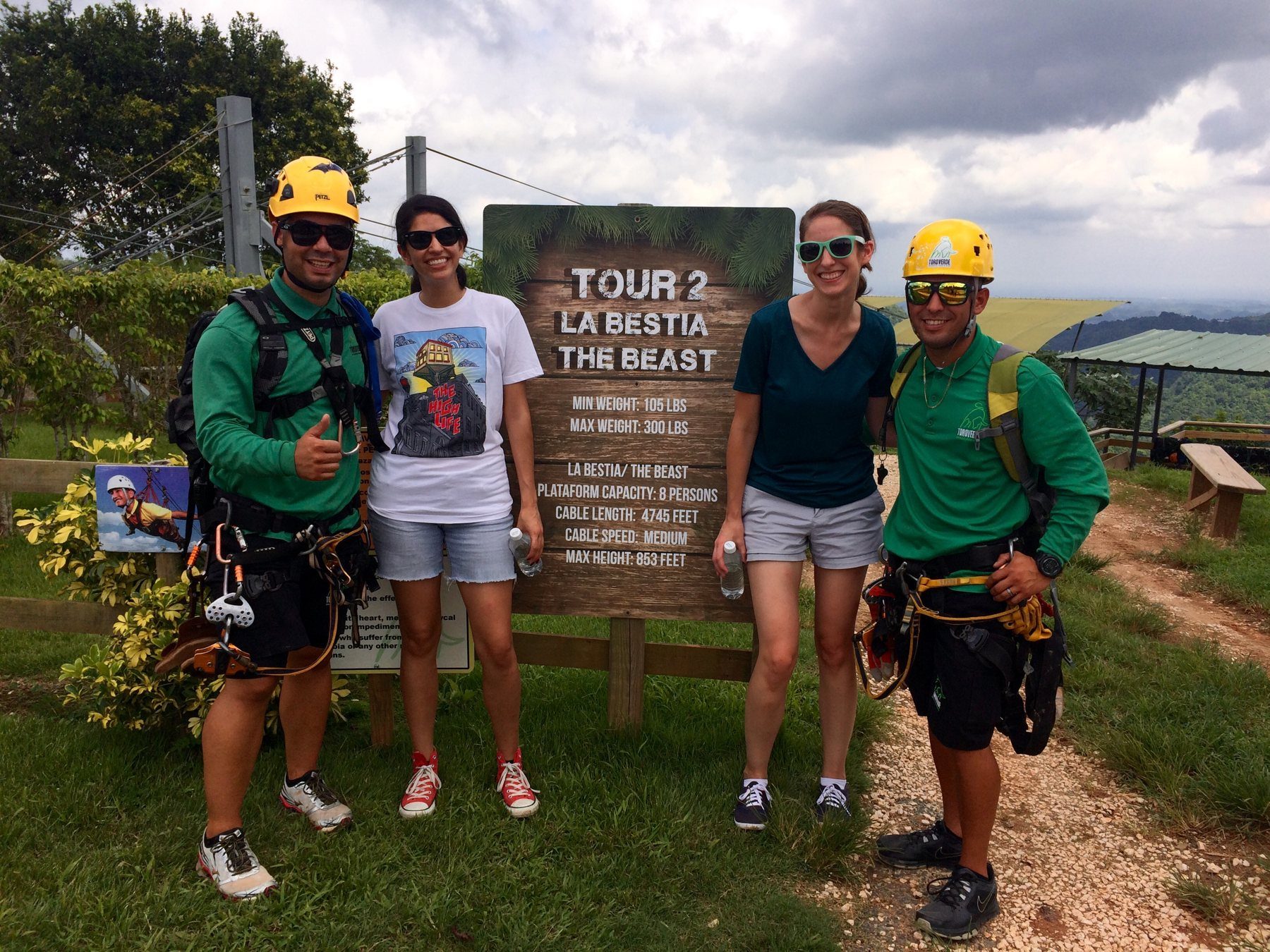 Two press-trip guests and two guides in climbing gear beside a 'Tour 2: La Bestia – The Beast' sign with mountains behind